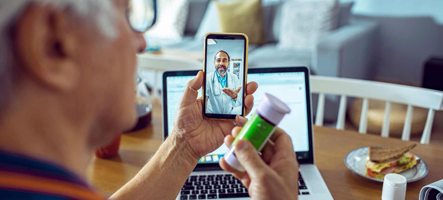 Patient holding a pill bottle and talking to a doctor through video call on his cell phone.